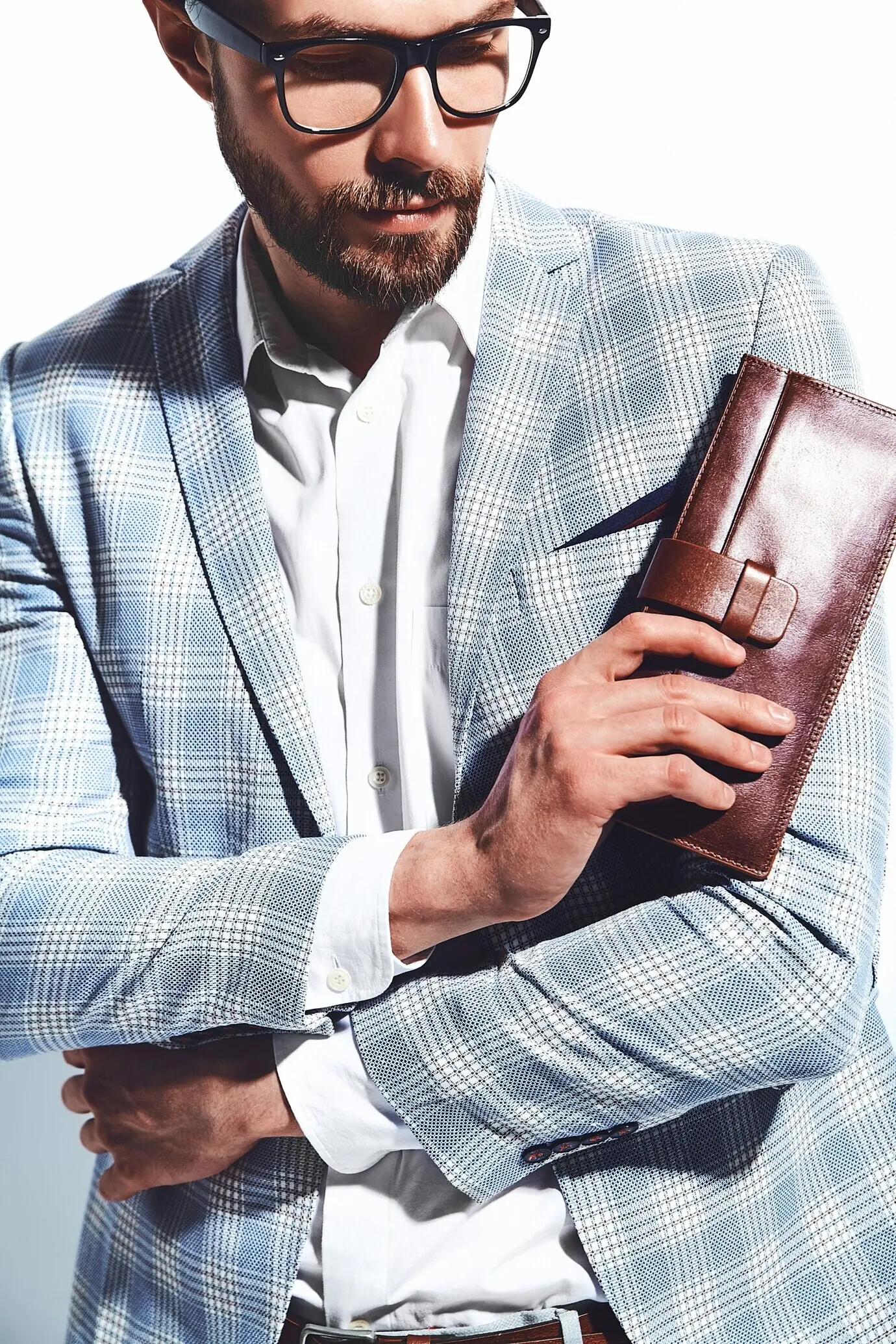 Портрет красивого модного стильного хипстера — бизнесмена-модели в элегантном светло-голубом костюме и очках на белом фоне.